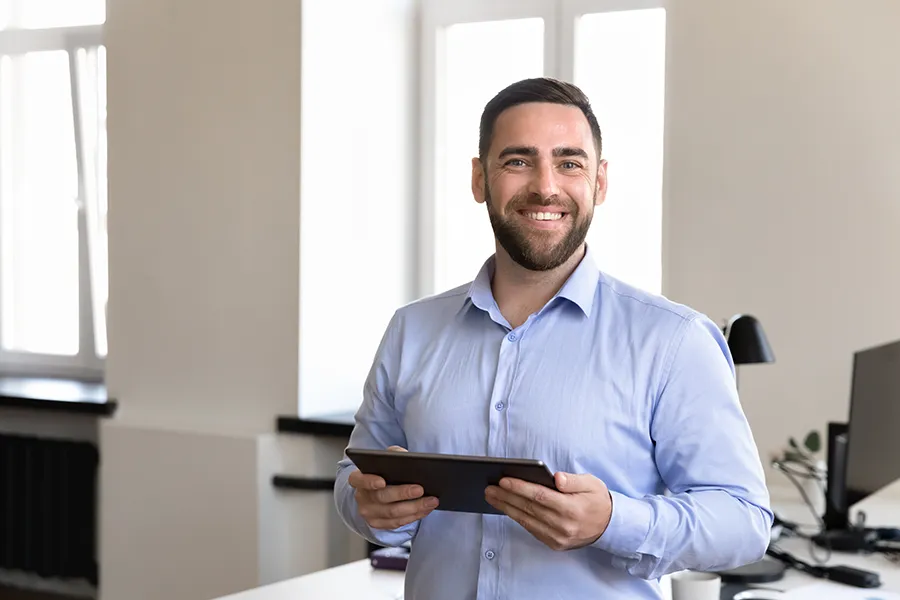 Smiling male Dynamics 365 consultant standing in an office holding a tablet device
