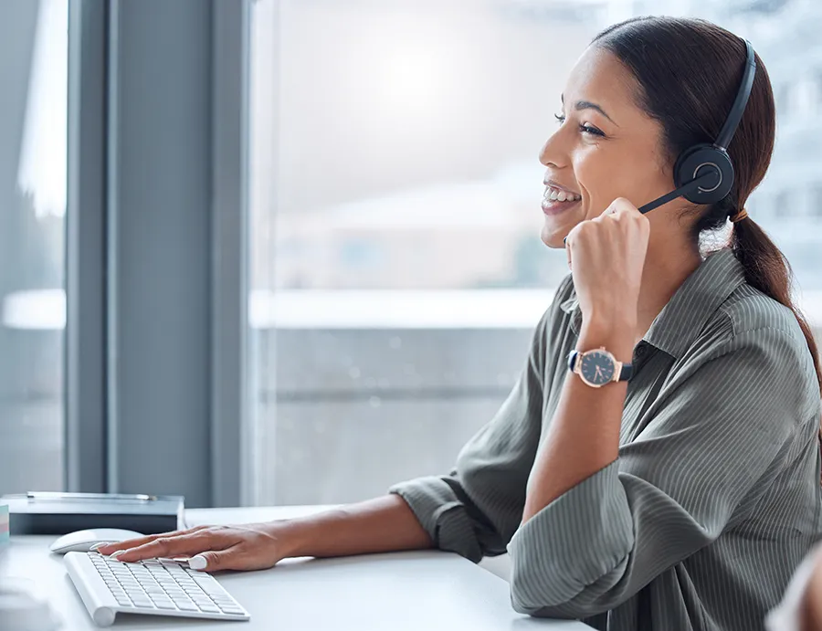 Female seller wearing a headset and smiling during a conversation and looking at Dynamics 365 Sales on a monitor.