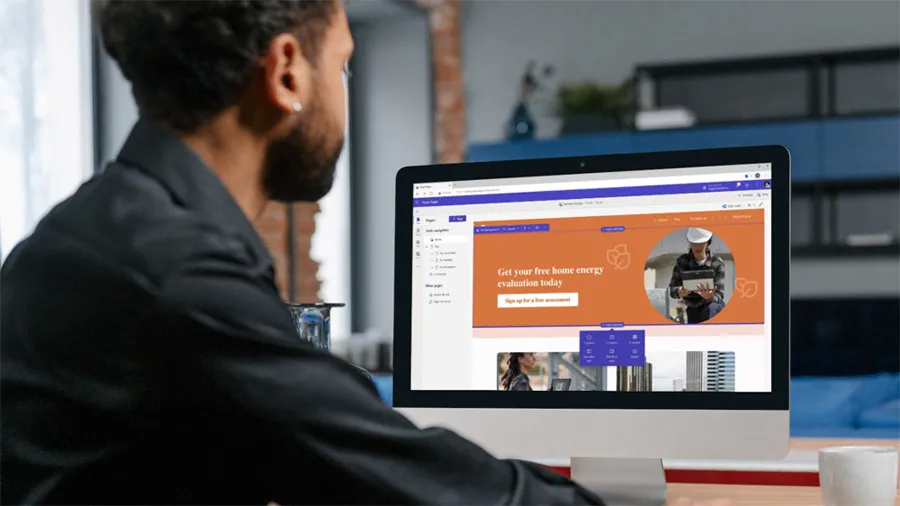 Photo of a young man seated behind a desk looking at a laptop screen displaying the Power Pages website designer.