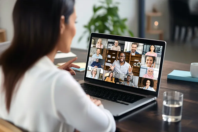 Rear camera shot of a woman seated at a home office desk engaged in a remote Dynamics CRM training session with co-workers.