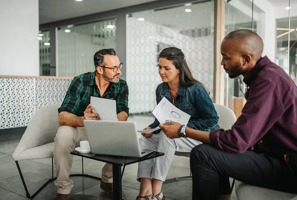 Wealth management consultant meeting two clients in an office and looking at a screen of Dynamics 365